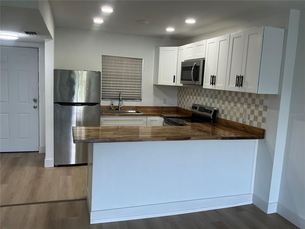 A kitchen features white cabinets, a wood countertop, stainless steel appliances, and a tiled backsplash — 2625 STATE ROAD 590 UNIT 2832, CLEARWATER, FL