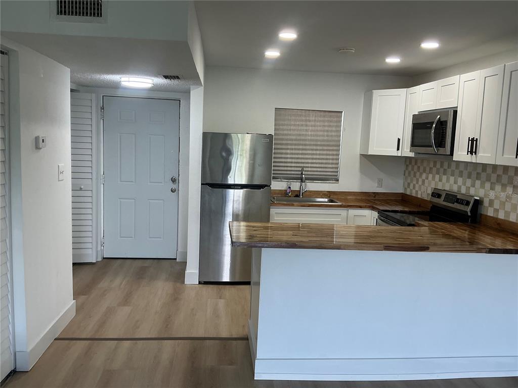 A kitchen features white cabinets, stainless steel appliances, and wood countertops with a breakfast bar — 2625 STATE ROAD 590 UNIT 2832, CLEARWATER, FL