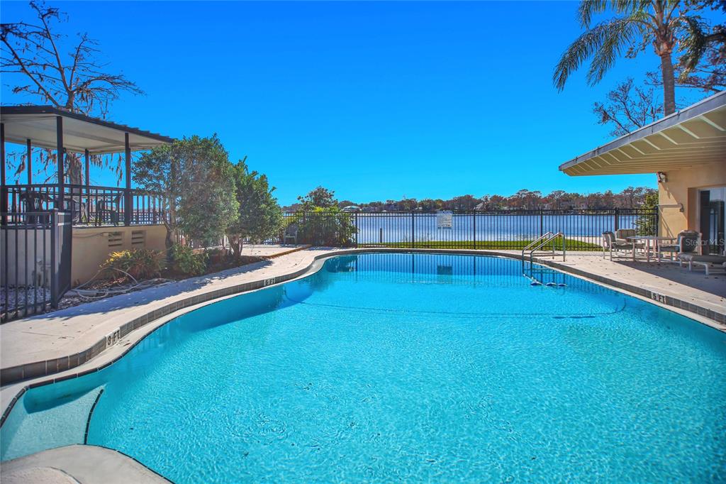 A swimming pool sits on a patio overlooking a lake with a fenced backyard — 2500 LEE RD. UNIT 222, WINTER PARK, FL