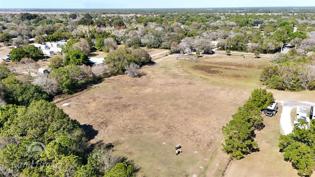 An aerial view shows a large, open grassy field surrounded by trees and residential structures — 448 NW 34TH STREET, OKEECHOBEE, FL