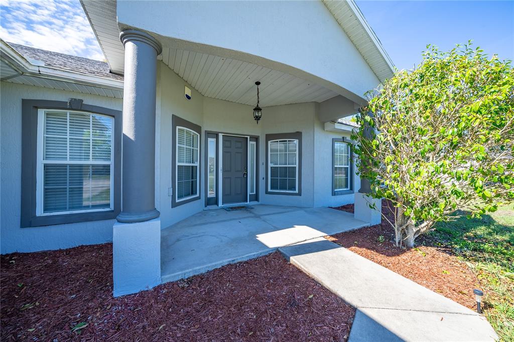 The front exterior of a house features a covered porch, gray door, and concrete walkway — 198 MALAUKA RUN, OCKLAWAHA, FL