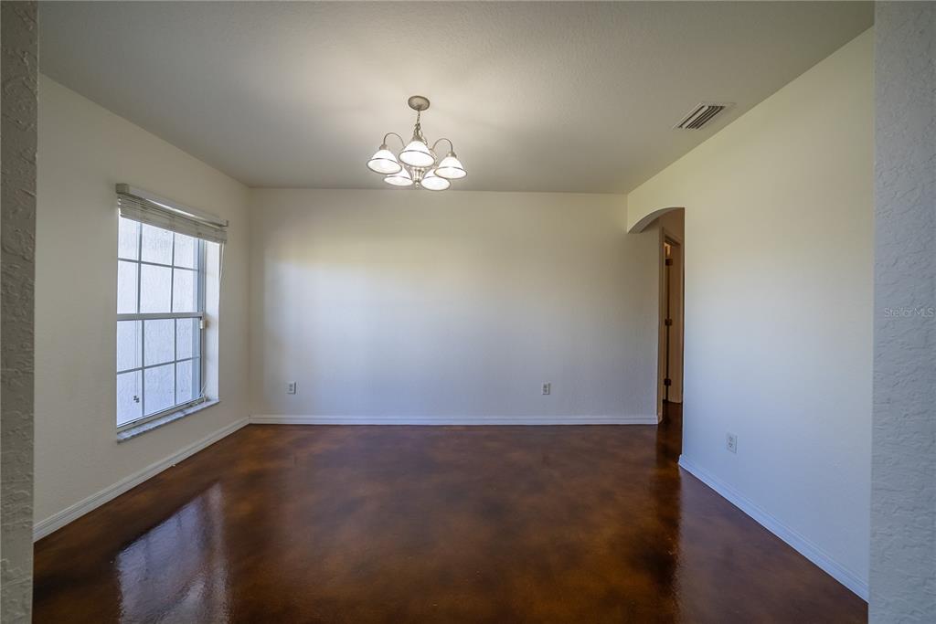 An empty dining room features a chandelier, a window with blinds, and stained concrete floors — 198 MALAUKA RUN, OCKLAWAHA, FL