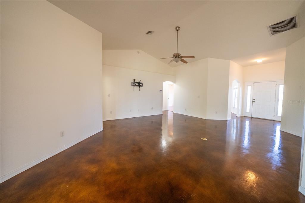 An empty living room features high vaulted ceilings, a ceiling fan, and stained concrete floors — 198 MALAUKA RUN, OCKLAWAHA, FL