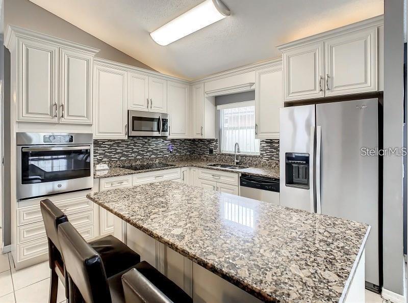 A kitchen features white cabinets, granite countertops, stainless steel appliances, and a central island — 9655 HOLLYHILL DRIVE, ORLANDO, FL