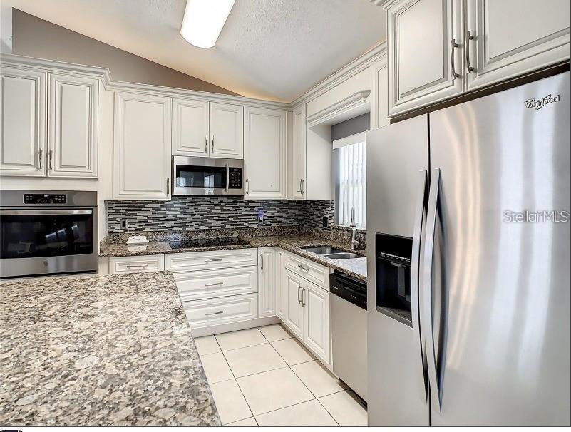 A kitchen features white cabinets, granite countertops, stainless steel appliances, and a tiled floor — 9655 HOLLYHILL DRIVE, ORLANDO, FL