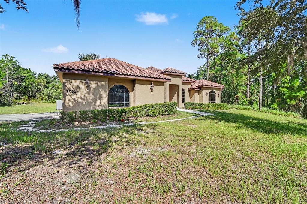 A single-story tan stucco house with a tile roof sits on a grassy lot — 2051 LORENE LANE, DELTONA, FL