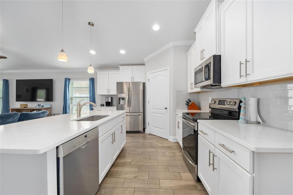 A modern kitchen features white cabinets, stainless steel appliances, a large island, and wood-look tile flooring — 64 COASTAL HAMMOCK WAY, ST AUGUSTINE, FL