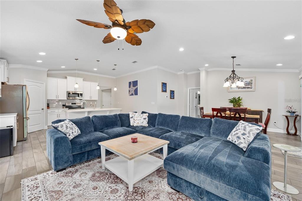 An open-concept living room features a large blue sectional sofa, a coffee table, and kitchen — 64 COASTAL HAMMOCK WAY, ST AUGUSTINE, FL