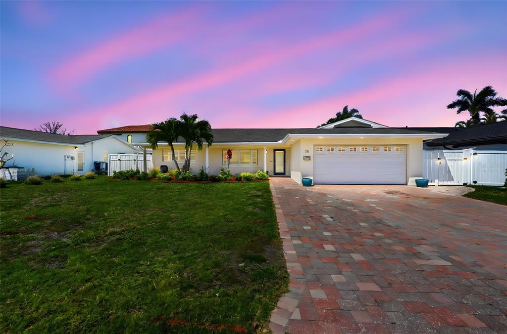 A single-story house with a brick driveway, two-car garage, and palm trees at sunset — 711 64TH AVENUE, ST PETE BEACH, FL