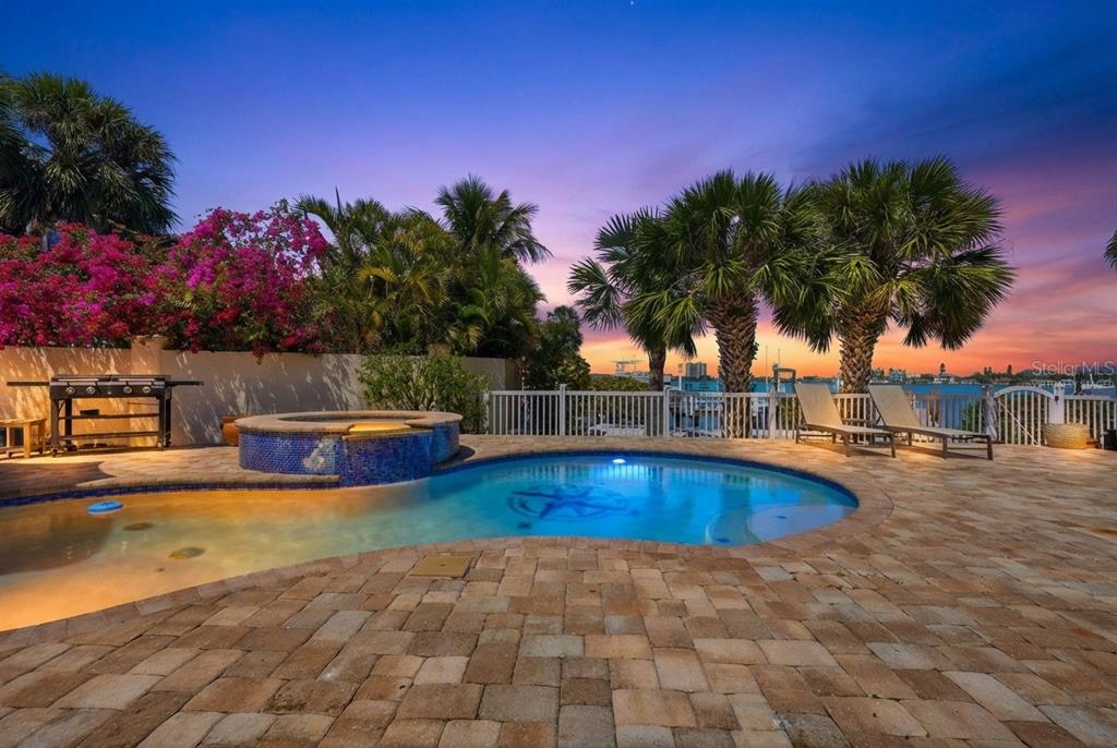 A backyard swimming pool and hot tub with a stone patio at sunset — 711 64TH AVENUE, ST PETE BEACH, FL