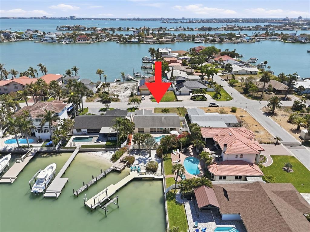 An aerial view shows a waterfront house with a pool, dock, and red arrow — 711 64TH AVENUE, ST PETE BEACH, FL