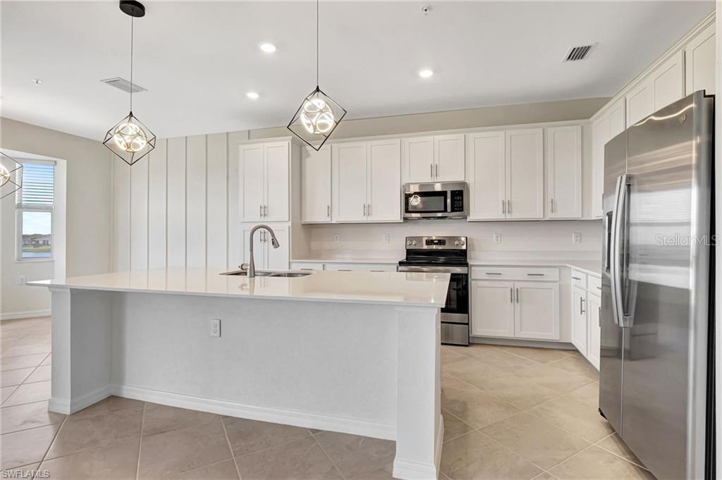A modern kitchen features white cabinetry, a large island with a sink, and stainless appliances — 5629 DOUBLE EAGLE CIRCLE UNIT 4242, AVE MARIA, FL
