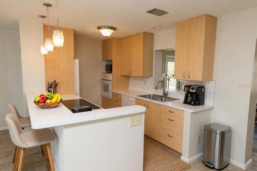 A kitchen with light wood cabinets, white countertops, stainless steel appliances, and a breakfast bar — 5864 MARIGOLD ROAD, VENICE, FL