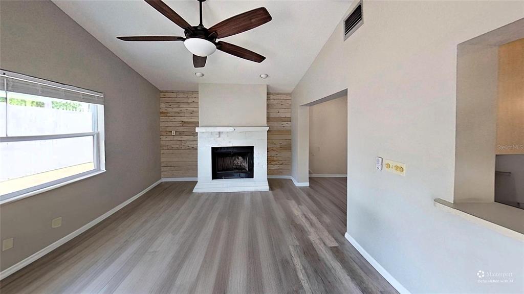 A living room features a fireplace with wood-plank accent walls, a ceiling fan, and flooring — 5864 MARIGOLD ROAD, VENICE, FL