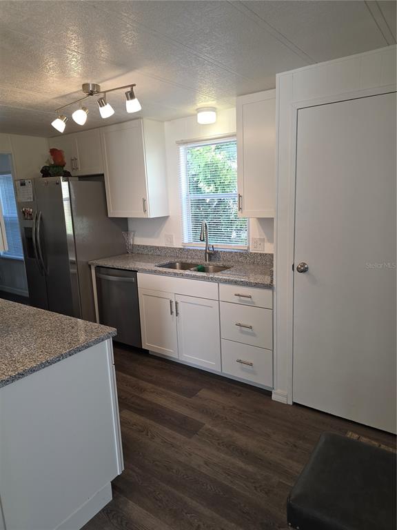 A kitchen with white cabinets, granite countertops, stainless steel appliances, and dark wood-look flooring — 102 BAREFOOT TRAIL, PORT ORANGE, FL