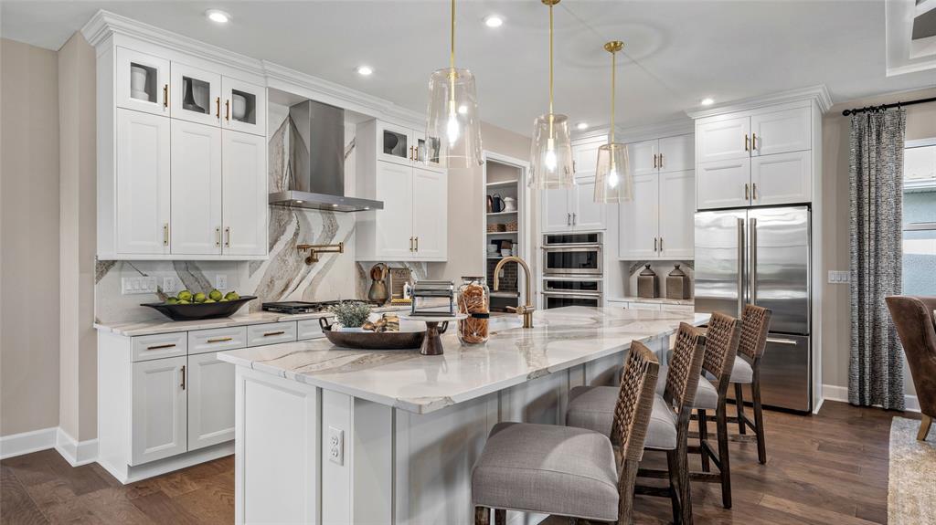 A modern kitchen features white cabinetry, a marble island, stainless steel appliances, and pendant lighting — 533 HAMMOCK OAKS BOULEVARD, LADY LAKE, FL