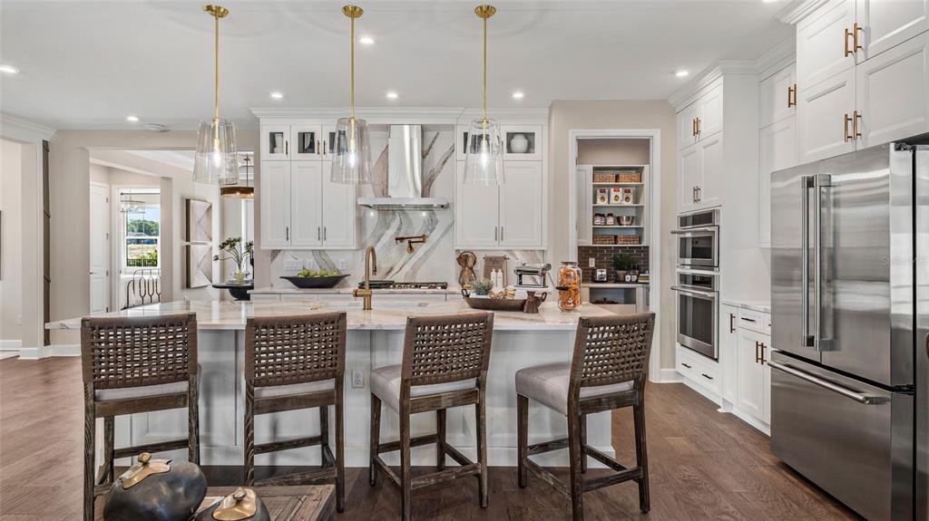 A modern kitchen features white cabinetry, a marble island with bar stools, and stainless appliances — 533 HAMMOCK OAKS BOULEVARD, LADY LAKE, FL