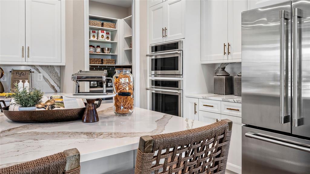 A modern kitchen features white cabinetry, a marble-topped island, and a walk-in pantry — 533 HAMMOCK OAKS BOULEVARD, LADY LAKE, FL