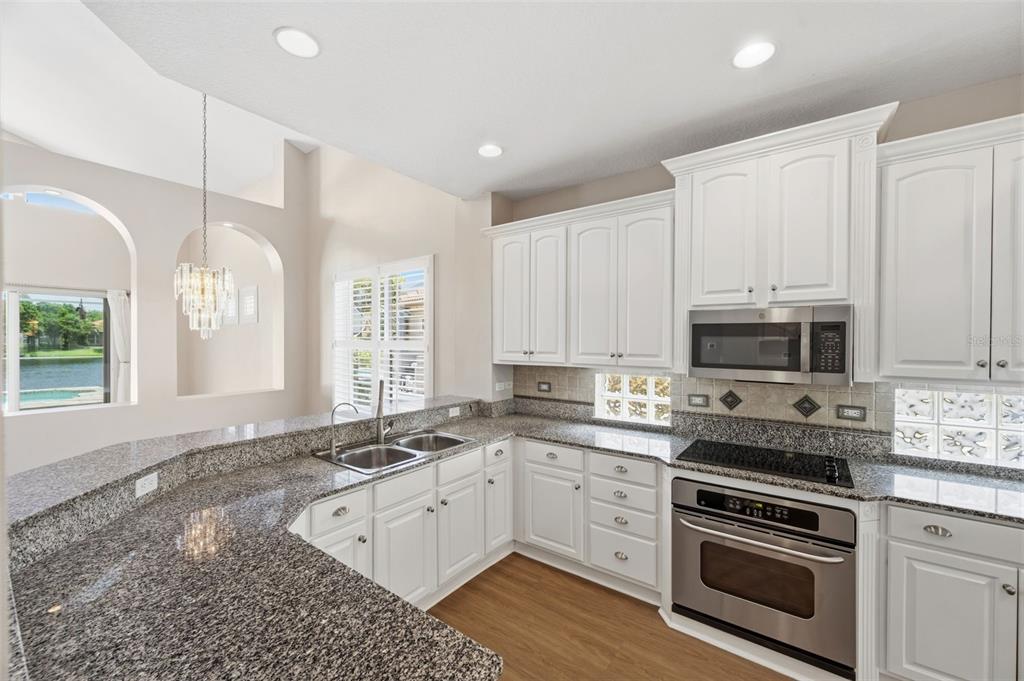 A kitchen features white cabinets, granite countertops, stainless steel appliances, and a view of water — 9985 SAGO POINT DRIVE, LARGO, FL