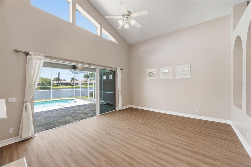 A living room with vaulted ceilings, wood-look flooring, and sliding glass doors opening to a pool — 9985 SAGO POINT DRIVE, LARGO, FL