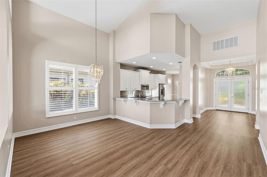 A dining area with wood-look flooring, a crystal chandelier, and an open kitchen with white cabinets — 9985 SAGO POINT DRIVE, LARGO, FL