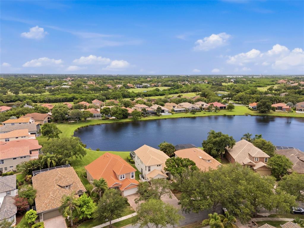An aerial view shows suburban houses with tile roofs surrounding a lake under a blue sky — 9985 SAGO POINT DRIVE, LARGO, FL
