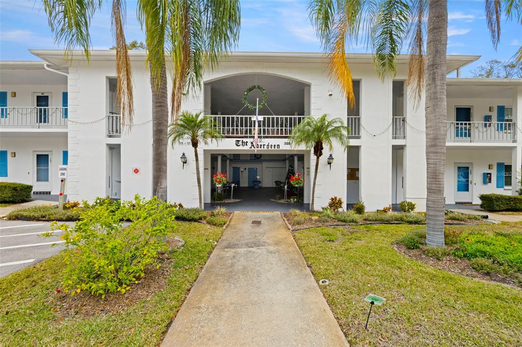 A two-story white apartment building with a central entrance and palm trees in front — 300 CLYDE LANE UNIT 106, DUNEDIN, FL