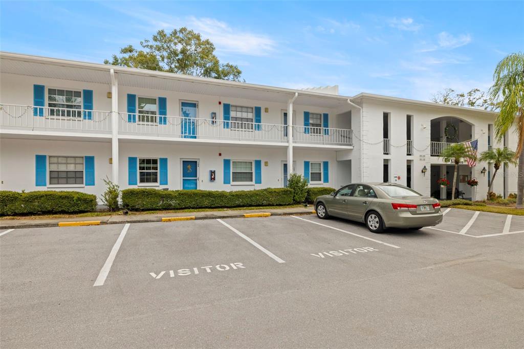 A two-story white apartment building with blue shutters and visitor parking spaces in front — 300 CLYDE LANE UNIT 106, DUNEDIN, FL