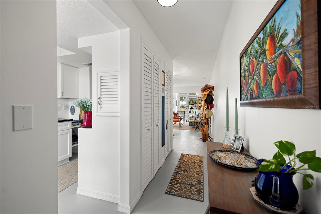 A hallway with white louvered closet doors leads toward a bright living area — 300 CLYDE LANE UNIT 106, DUNEDIN, FL