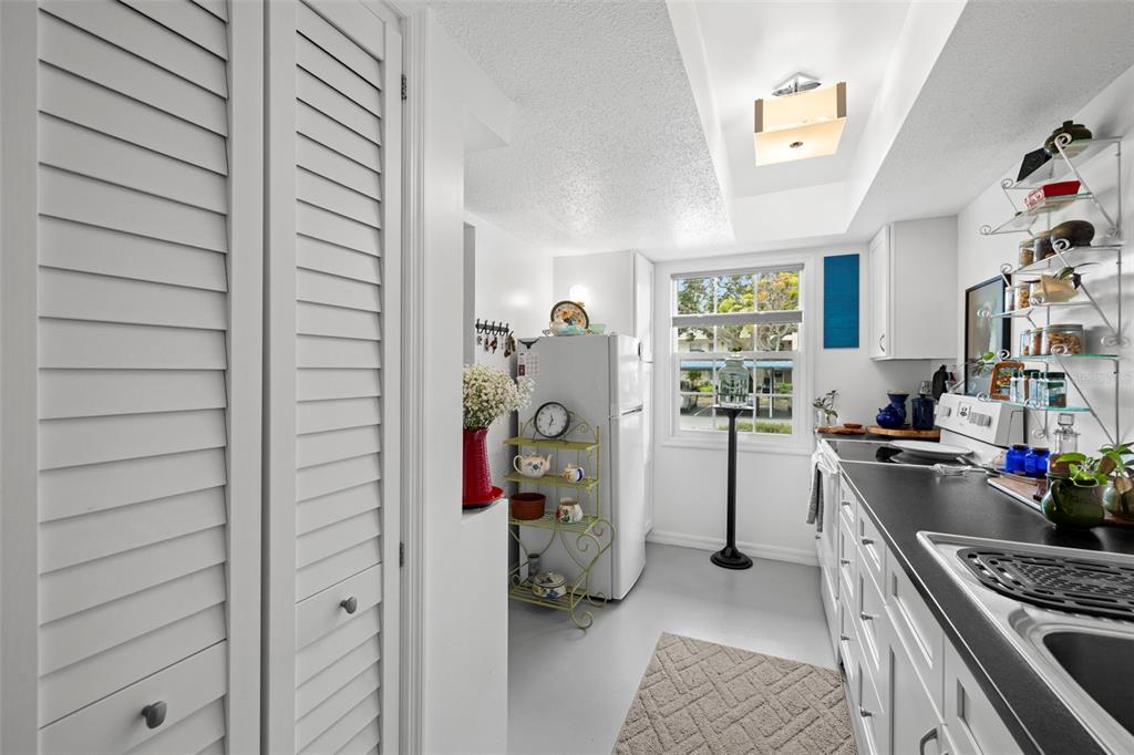 A white kitchen features louvered closet doors, a black countertop, and a window with exterior views — 300 CLYDE LANE UNIT 106, DUNEDIN, FL