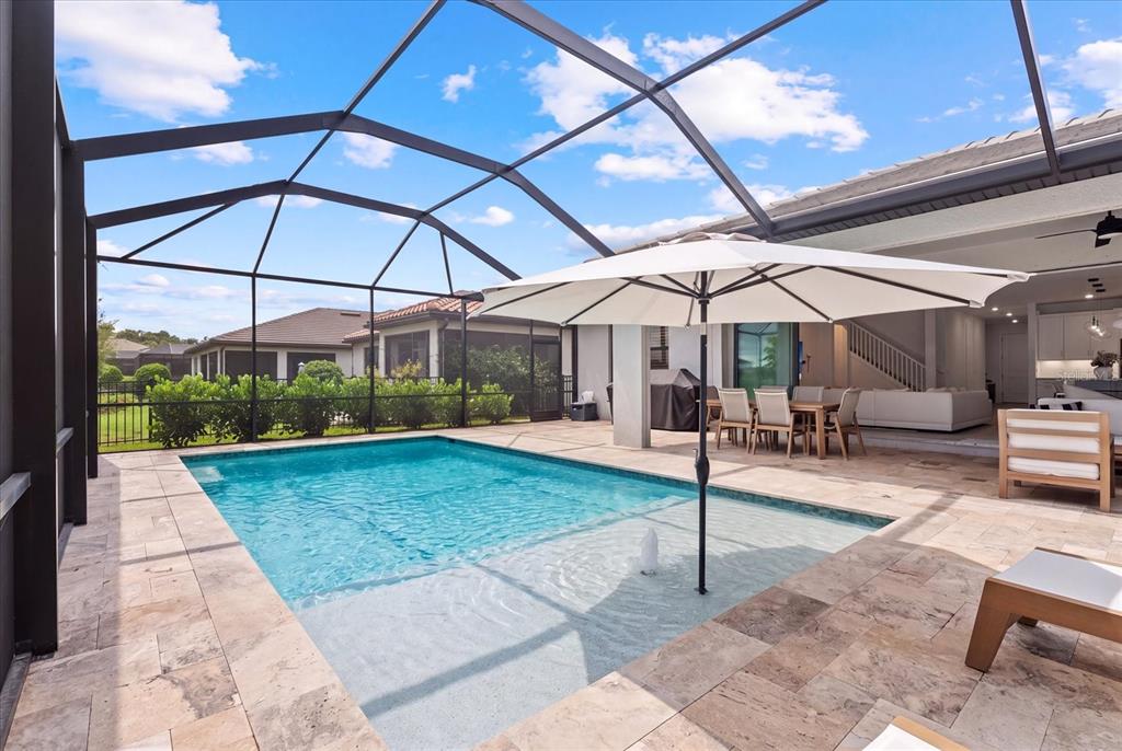 A screened-in patio features a swimming pool with a tanning ledge and an outdoor umbrella — 725 GADWALL COURT, BRADENTON, FL