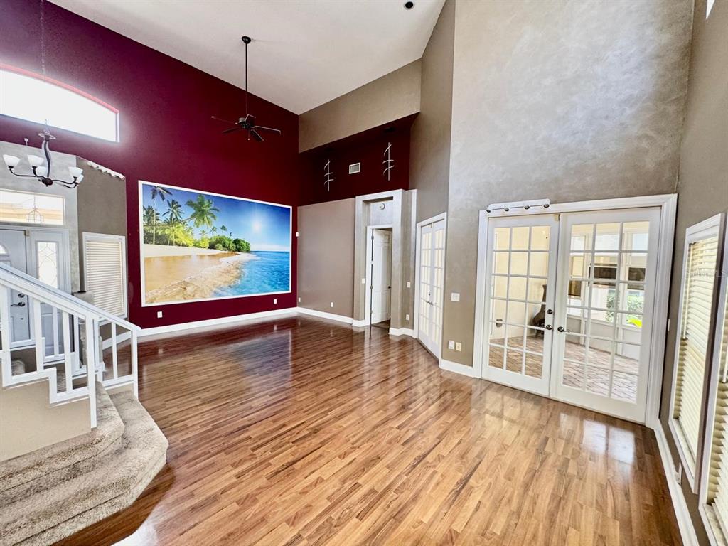 A high-ceilinged living room features hardwood floors, a large beach mural, and French doors — 5121 FAIRWAY ONE DRIVE, VALRICO, FL