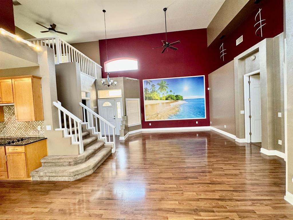 A high-ceilinged living room features wood flooring, a carpeted staircase, and a large beach mural — 5121 FAIRWAY ONE DRIVE, VALRICO, FL