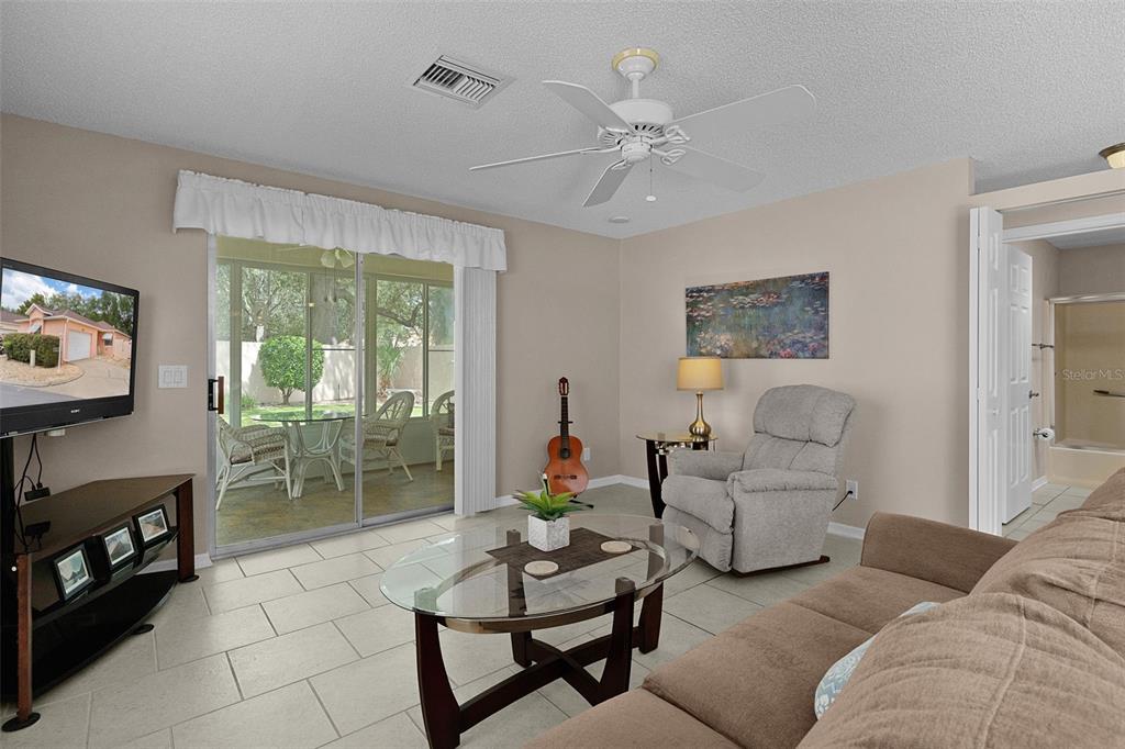 A living room features tile floors, a ceiling fan, a glass coffee table, and sliding doors — 1023 AVALON AVENUE, THE VILLAGES, FL