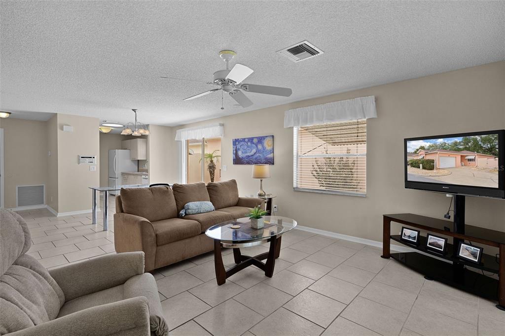 A living room with tile floors, a brown sofa, a glass coffee table, and a television — 1023 AVALON AVENUE, THE VILLAGES, FL