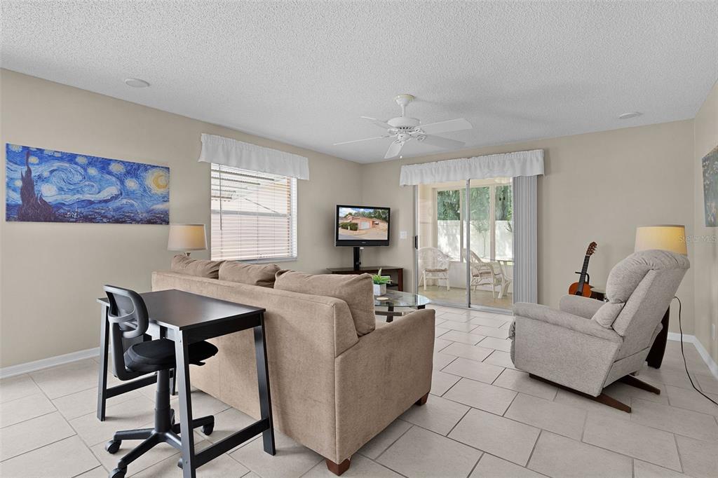 A living room with tile floors, a beige sofa, a recliner, and a sliding glass door — 1023 AVALON AVENUE, THE VILLAGES, FL