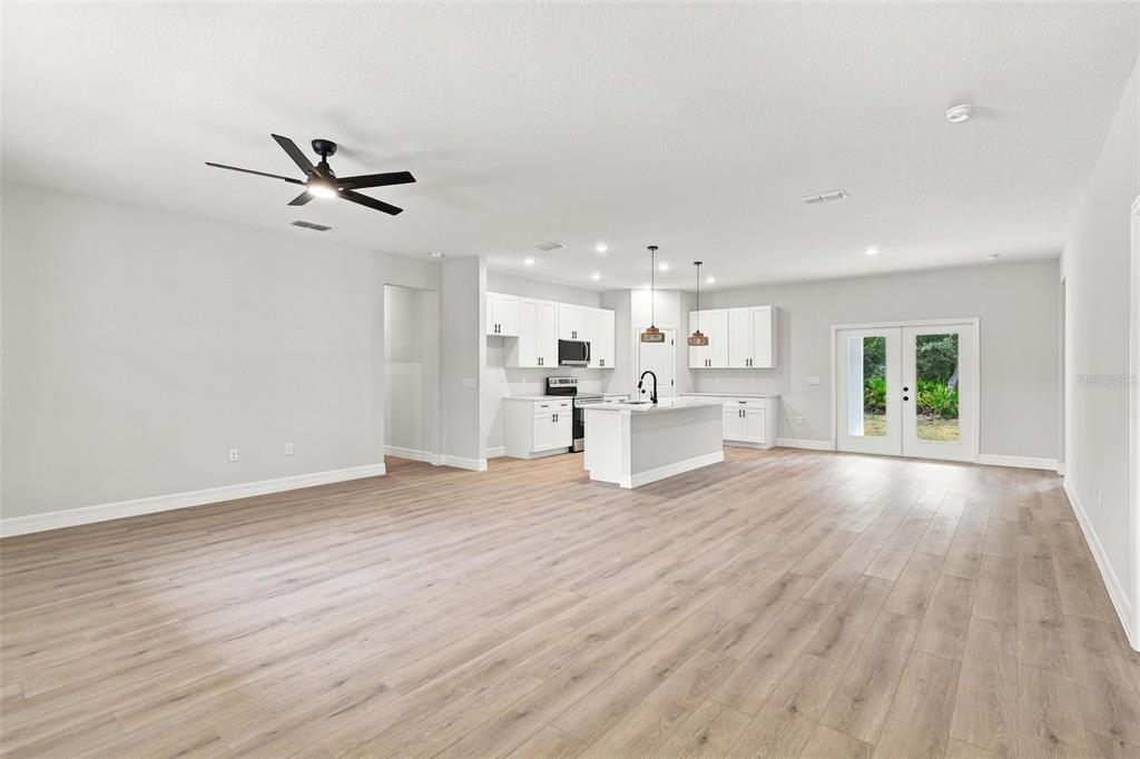 An open-concept living area features light wood-look flooring, a white kitchen with an island, and doors — 41325 ROYAL TRAILS ROAD, EUSTIS, FL
