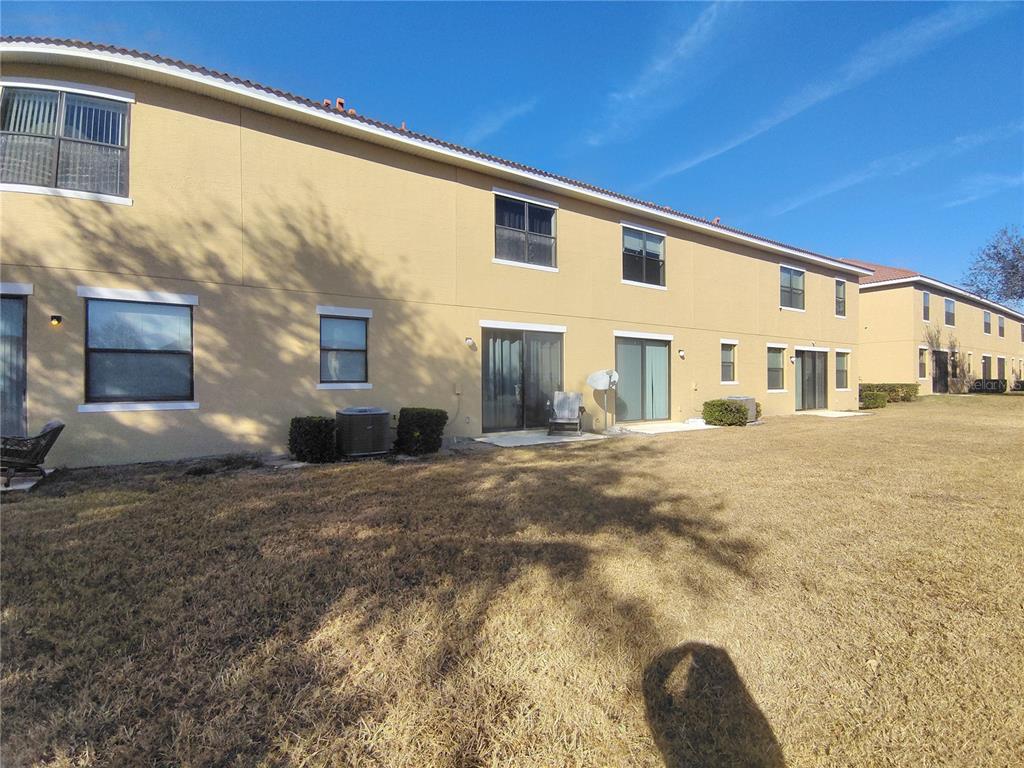 The exterior rear view of a two-story tan townhouse with a grassy backyard — 1423 PACIFIC ROAD, POINCIANA, FL