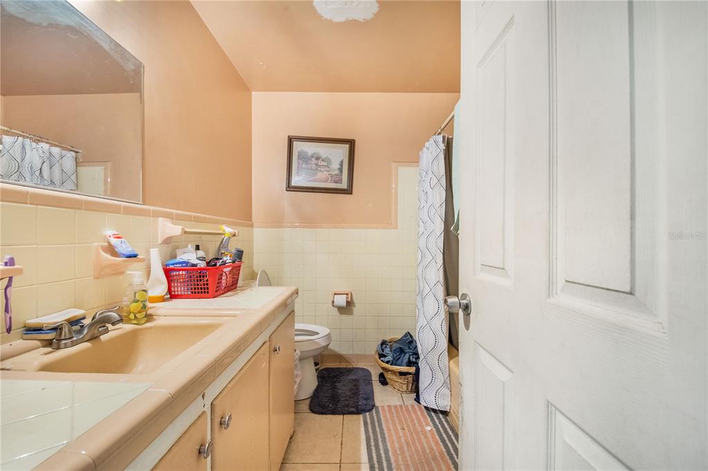 A bathroom features a peach-colored vanity, tiled walls, a shower curtain, and a toilet — 400 E POMELO STREET, LAKE ALFRED, FL