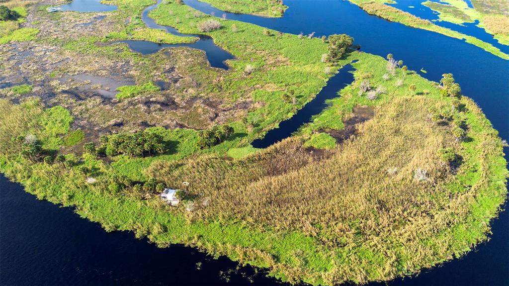An aerial view shows a small cabin situated on a grassy island surrounded by water — NO NAME, OSTEEN, FL