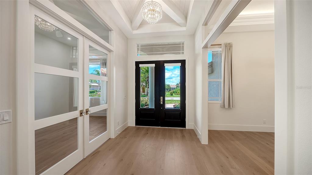 An open-concept living area with light wood floors, a modern chandelier, and large glass doors — 2729 HARVEST DRIVE, SARASOTA, FL
