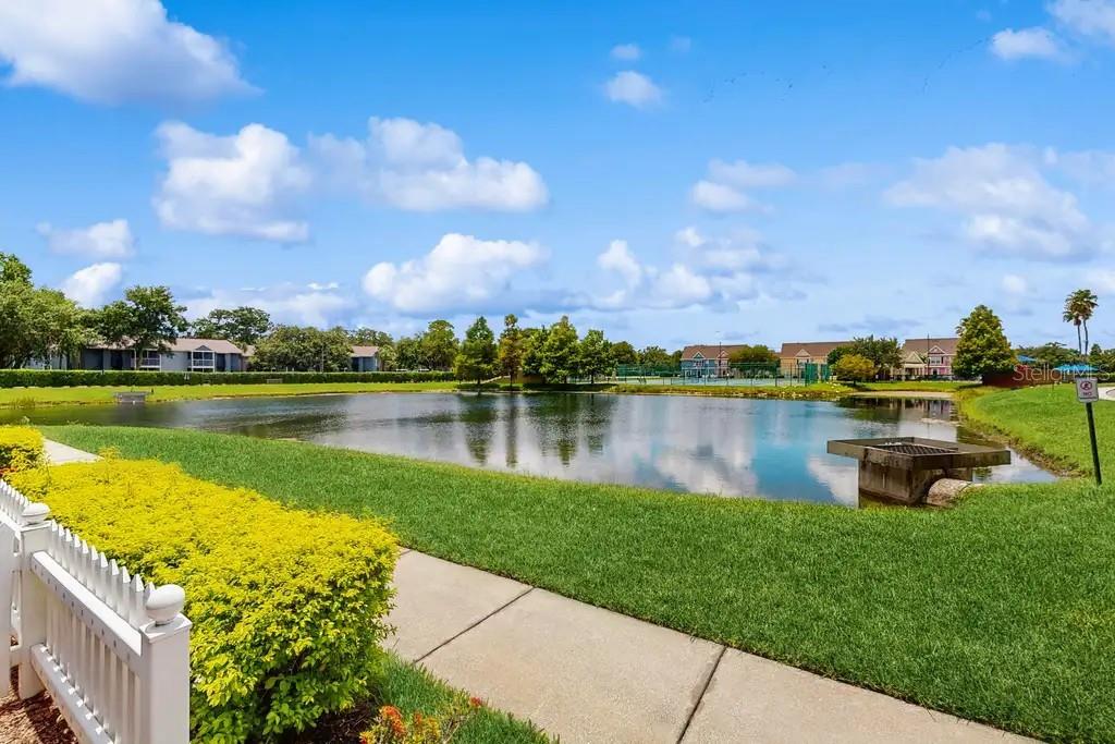 A view of a pond with a concrete drainage structure and a grassy lawn — 2200 SAN VITTORINO CIRCLE UNIT 105, KISSIMMEE, FL
