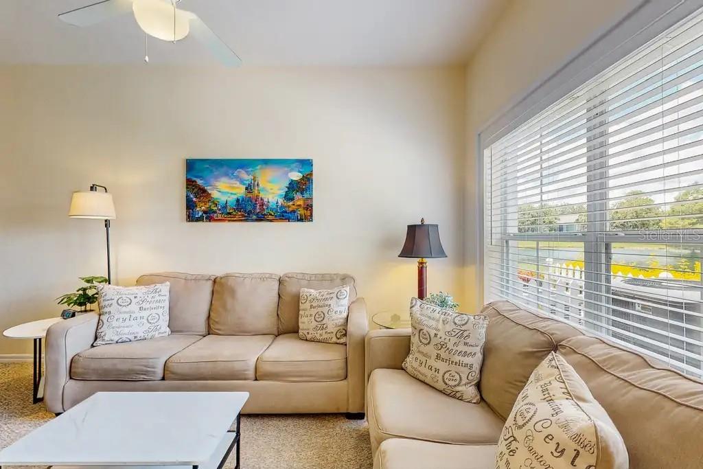 A living room features two beige sofas, a coffee table, and a colorful castle wall art — 2200 SAN VITTORINO CIRCLE UNIT 105, KISSIMMEE, FL