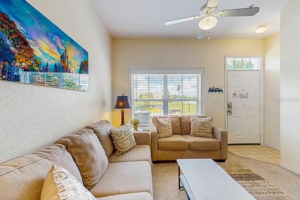 A living room features a beige sectional sofa, a loveseat, a coffee table, and wall art — 2200 SAN VITTORINO CIRCLE UNIT 105, KISSIMMEE, FL