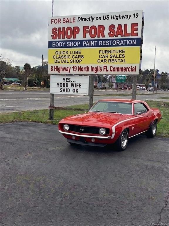 A red classic Chevrolet Camaro SS is parked in front of a commercial for-sale sign — 8 HIGHWAY 19 N, INGLIS, FL
