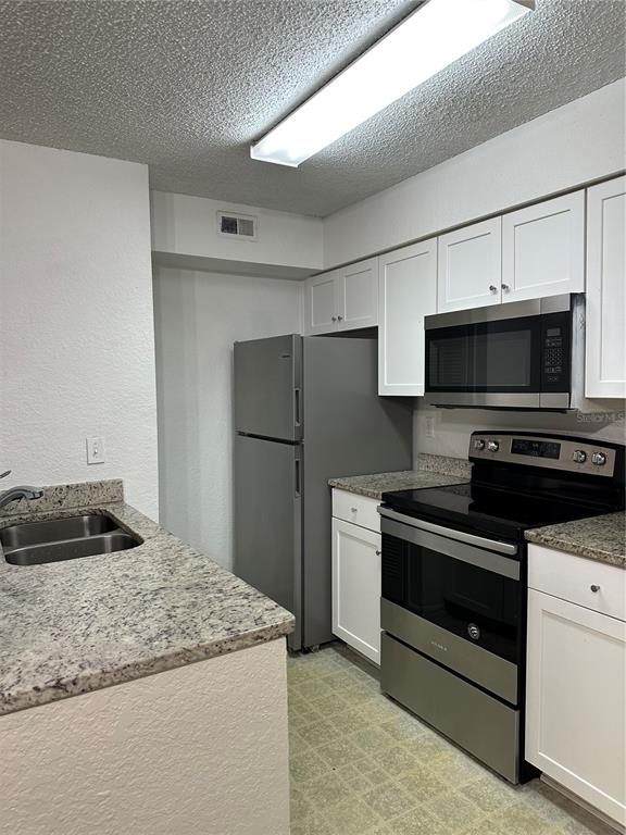 A kitchen features white cabinets, stainless steel appliances, and speckled granite countertops — 2214 METROPOLITAN WAY UNIT 1022, ORLANDO, FL