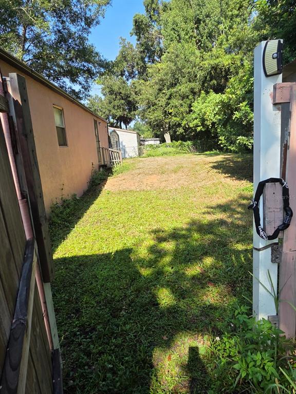 A view from a gate looking toward a grassy backyard beside a peach-colored house — 18341 12TH AVENUE, ORLANDO, FL