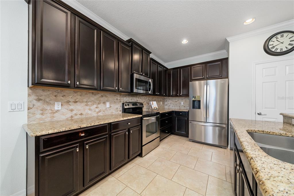 A kitchen features dark wood cabinets, granite countertops, stainless steel appliances, and a tiled backsplash — 2202 REDMARK LANE, WINTER GARDEN, FL