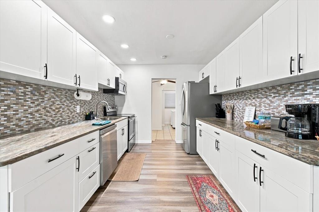 A galley kitchen features white cabinets, stainless steel appliances, and a mosaic tile backsplash — 6350 60TH AVENUE N, ST PETERSBURG, FL