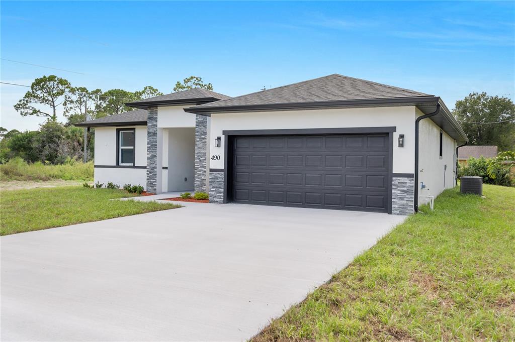 A single-story house with a white stucco exterior, dark trim, and a two-car garage — 490 CAROLINA AVENUE NW, PALM BAY, FL